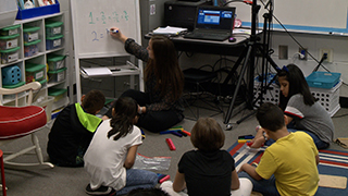  kids sitting on the floor watching teacher