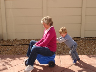 Child Pushing Grandmother on Plastic Tricycle 