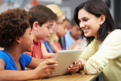 students using tablet and talking to an adult 