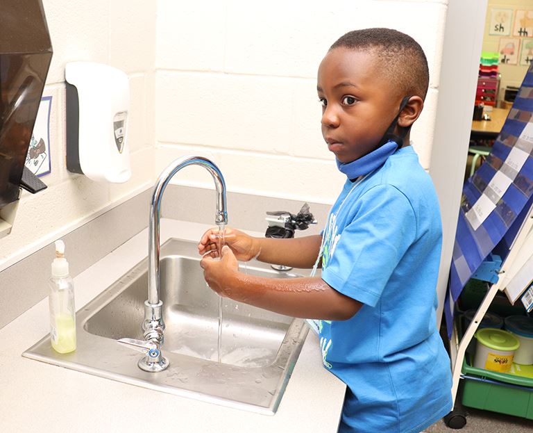 Kindergarten student washes hands at sink
