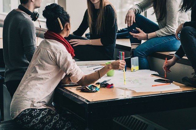 Studying - A group of students gather around a table covered with papers to study and discuss 